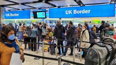 A photograph of passport control at an airport in the United Kingdom. Queues of people are waiting in line to gain entry into the United Kingdom. 