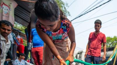 Indian woman holding hose attached to water tanker