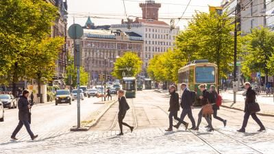 A photograph of a busy street in Finland, with people crossing a tram line in a city.
