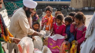 A photograph from New Delhi, India in 2021. A man in a white turban can be seen donating wheat flour to young girls in a slum.